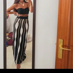 Stickad långkjol med vågiga ränder - Säljer en svart och vit stickad långkjol med vågiga vertikala ränder och bred resår i midjan. Kjolen har en unik struktur med inslag av beige och är perfekt för dig som gillar statement-plagg med cool design.