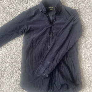 Mörkblå manchester-skjorta Massimo Dutti - Snygg mörkblå skjorta från Massimo Dutti i mjuk manchester. Klassisk krage med knappar och långärmad design. Perfekt att bära över en t-shirt för en chill och stilren look. Skjortan har en normal passform och är tillverkad av ett slitstarkt tyg.