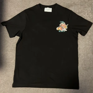 Svart Casablanca t-shirt med tryck - Casablanca t-shirt i svart med färgstarkt grafiskt tryck fram och bak, där texten 'CASA BLANCA' syns tydligt. T-shirten har rund hals och korta ärmar. Tillverkad i 100% ekologisk bomull för skön känsla och snygg passform.
