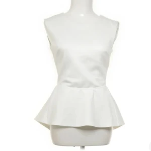 Vit peplumtop från AX Paris - Snygg vit peplumtop från AX Paris med ärmlös design och rund hals. Toppen har en öppen rygg med knappstängning upptill och är tillverkad i mjuk polyester med lite stretch för skön passform. Perfekt för dig som gillar stilrena och trendiga plagg.