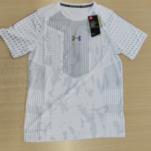 Vit Under Armour t-shirt med mönster - Snygg vit t-shirt från Under Armour med coolt geometriskt och randigt mönster i grått. T-shirten har korta ärmar och är gjord i lätt polyester som andas, perfekt för träning. Loggan syns både fram och bak i olika färger. Skön passform och sportig vibe.
