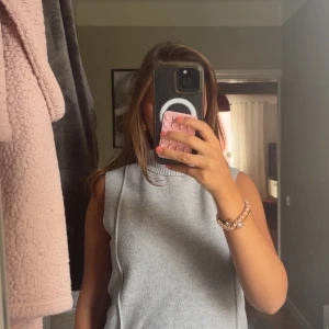 Grå stickad väst med polokrage - Snygg grå stickad väst med bred polokrage och ribbade detaljer. Modellen är ärmlös och har en rak, loose passform som ger en chill vibe. 