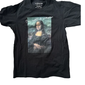  t-shirt med Mona Lisa-tryck  - Svart t-shirt från Pull&Bear med stort tryck av Mona Lisa och texten 'I'm not a poser' på bröstet. Klassisk rund hals och korta ärmar. Perfekt statement-plagg för dig som gillar konst och streetstyle.