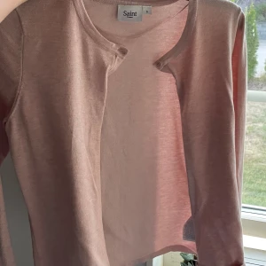 Ljusrosa kofta från Saint Tropez - Säljer en ljusrosa kofta från Saint Tropez i storlek S. Koftan har rund hals, långa ärmar och knappar framtill. Materialet är mjukt och tunt, perfekt för lager-på-lager. Enkel och stilren design som funkar till många olika outfits.
