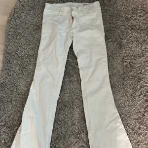 Vita bootcut byxor med låg midja - Snygga vita byxor med bootcut-modell och låg midja. Byxorna har klassiska fickor fram och bak samt hällor för bälte. Perfekta för dig som gillar en stilren och fräsch look. Materialet känns mjukt och följsamt.