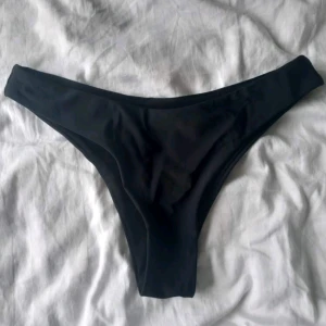 Svarta bikiniunderdel - Snygg svart bikiniunderdel med enkel design. Modellen har högt skurna ben och en tight passform som framhäver siluetten. Perfekt för strandhäng eller poolparty. Materialet känns mjukt och följsamt mot huden. Passar även S! 