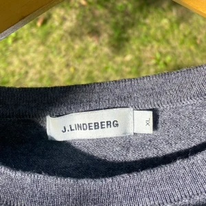 Grå stickad tröja från J.Lindeberg - Säljer en stilren grå stickad tröja från J.Lindeberg i storlek XL barn storlek, så passar längden 165-175. Använd ett fåtal gånger, inga skavanker!