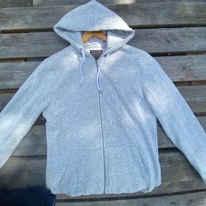 Ljusgrå hoodie med dragkedja - Snygg ljusgrå hoodie med hel dragkedja och vita snören i huvan. Inga skavanker