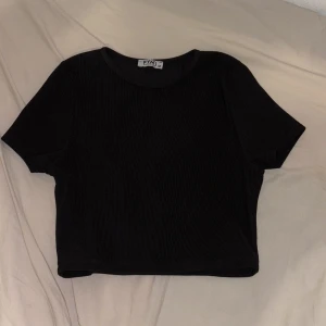 Svart ribbad croppad topp  - En svart, croppad topp från FYM med korta ärmar och rund hals. Toppen är ribbad och har en enkel, stilren look som passar perfekt till jeans eller kjol. Materialet är mjukt och stretchigt för en bekväm passform så det går även bra för dig som har storlek S💕 Anvönd en gång 