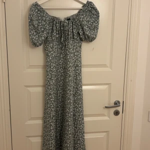 Blommig långklänning med puffärm - Supersöt långklänning med blommigt mönster och puffiga kortärmar. Finns i grönt, rött och blått med vita blommor. Klänningen har offshoulder och snörning vid halsen, samt en slits framtill för extra flow. Perfekt för sommarens alla tillfällen! Alla för 299kr!