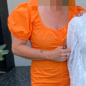 Orange kort klänning från Ganni - Säljer en superfin orange kort klänning från Ganni med puffärmar och snygg rynkning längs hela klänningen. Modellen har rundad halsringning och snörning framtill. Perfekt för dig som vill sticka ut med färg! Materialet är bomull och passformen är normal.