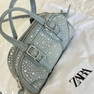 Glittrig ljusblå handväska från Zara - Kanske är intresserad av att sälja min skit snygg ljusblå handväska från Zara i jeansmaterial med glittriga paljetter över hela väskan som inte säljs längre. Den är i Mycket bra skick och har original påsen till. Väskan har en pytteliten fläck som man ser på sista sidan men som säkert går bort har inte testat. Väskan har två handtag, justerbar axelrem och silverfärgade spännen. En ficka i själva väskan. Hör av dig om du har frågor eller funderingar, pris kan diskuteras💕💕