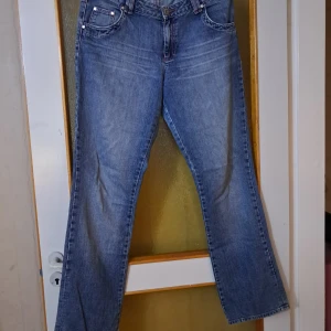 Blå bootcut jeans från Lindex - Snygga blå jeans från Lindex med bootcut-modell och klassisk femficksdesign. Jeansen har rosa kontrastsömmar och broderade blommor på ena bakfickan som ger en unik touch. Tillverkade i mjukt denimtyg med normal passform. Fint skick :)