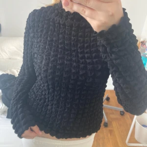 Svart strukturerad tröja - Säljer en svart tröja med unik bubblig struktur och vågiga kanter vid ärmslut och nederkant. Tröjan har lång ärm och en lite loose passform, perfekt för dig som vill ha något annorlunda och mysigt i garderoben.