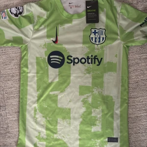 FC Barcelona matchtröja Nike - Säljer en FC Barcelona matchtröja från Nike med klassiska blå och röda vertikala ränder, gula detaljer och klubbmärke på bröstet. Tröjan har gul rund halsringning, Rakuten-tryck på framsidan och är tillverkad i lätt polyester. Perfekt för dig som älskar Barca!