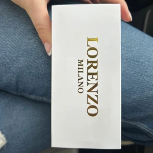 Guldig rektangulär klocka Lorenzo Milano - Stilren klocka från Lorenzo Milano med rektangulärt ur och klassisk länk i guldton. Vit urtavla med romerska siffror och diskret logga. Perfekt accessoar för dig som gillar en elegant och tidlös look.