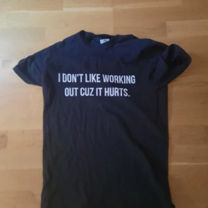 Svart t-shirt cookie merch  - Svart t-shirt med vit text på bröstet: 'I DON'T LIKE WORKING OUT CUZ IT HURTS.' Klassisk rund hals och korta ärmar. Perfekt för dig som gillar humor och vill sticka ut med ett statement-plagg. Mjuk och skön känsla, passar till jeans eller shorts.