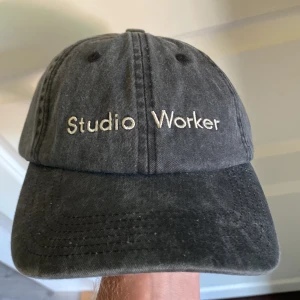 Svart keps Studio Worker Pica Pica - Snygg svart keps från Studio Worker x Pica Pica i tvättad bomull. Broderad text framtill och justerbart spänne bak för perfekt passform. Enkel och stilren design som passar till allt. Perfekt accessoar för en chill look.