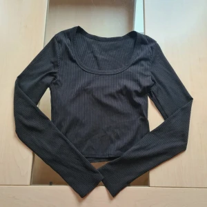 Svart ribbad långärmad topp - Svart långärmad topp från Shein i ribbad polyester. Modellen är croppad med rundad urringning och smal passform. Perfekt att styla med höga jeans eller kjol för en clean look.