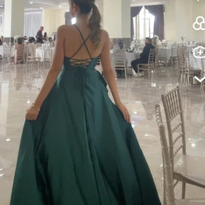 Mörkgrön långklänning med snörning - Elegant mörkgrön långklänning med vackert fall och slits framtill. Klänningen har smala axelband, snörning i ryggen och en draperad urringning. Perfekt för dig som vill sticka ut med en stilren och sofistikerad look. Funkar för xs och s