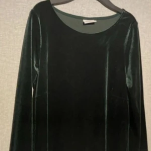 Mörkgrön sammetklänning från Vila - Snygg mörkgrön klänning i mjuk sammet från Vila. Klänningen har långärmade och en rund halsringning, vilket ger en stilren och elegant look. Perfekt för dig som vill sticka ut med en djup grön färg och lyxig känsla.