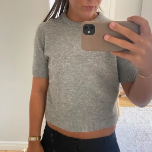 Grå stickad kortärmad tröja - Säljer en enkel och snygg grå stickad tröja med korta ärmar. Modellen är lite croppad och har ribbade kanter vid ärmslut och nederkant. Perfekt för dig som gillar stilrena och mjuka plagg. Kommer även från Zara🥰