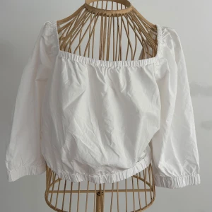 Vit croppad blus med puffärm från Lindex - Superfin vit blus från Lindex med bred, fyrkantig urringning och puffiga trekvartsärmar. Modellen är croppad med resår i både ärmslut och nederkant. Tillverkad i 100% bomull för en luftig och skön känsla. Perfekt för en trendig och avslappnad look. Aldrig använd.