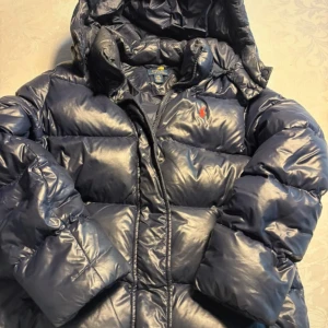 Ralph lauren jacka - Skitsnygg populär jacka från ralph lauren som typ inte finns längre. Perfekt nu till hösten och vintern! Verkligen så skön. Den är marinblå och har en glansig yta, även märket på vänster sida. Köpte på vinted men passade tyvärr inte💔nypris 3-4 tusen. Strl 12-14 år och skulle säga att den passar xxs-s, men var lite för kort i armarna för mig som är 173.