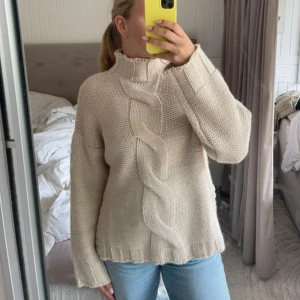 Beige stickad polotröja med fläta - Säljer en beige stickad polotröja med grov fläta både fram och bak. Tröjan har hög krage, lång ärm och en loose fit. 