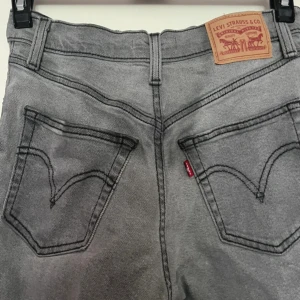 Levi's Ribcage Straight Ankle jeans grå - Grå Levi's Ribcage Straight Ankle jeans med hög midja och raka ben. Klassisk femficksmodell med svarta kontrastsömmar och ikonisk läderpatch bak. Jeansen är i ett mjukt denimtyg och har knappgylf. Perfekta för en clean och stilren look.