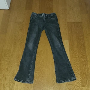 Svarta bootcut jeans Gina Tricot  - Snygga svarta jeans från Gina Tricot i storlek 152. Modellen har bootcut-ben med lätt utsvängning och klassisk femficksdesign. Jeansen är gjorda i mjukt denimtyg och har en mörk tvätt med subtila slitningar för en cool look.