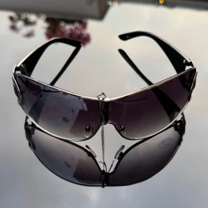 NYA Svarta solglasögon  - Säljer ett par riktigt snygga svarta NYA solglasögon med breda skalmar och stora silverfärgade. Glasen är tonade och har en sportig, rundad form som ger cool vibe. Hämtas i Hägersten. 