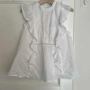 Vit blus från Bik Bok XS - Supersöt vit blus från Bik Bok i storlek XS. Blusen har volanger längs sidorna, smockad halsringning och fina veckade detaljer framtill. Ärmlös design med spetskantade volanger och ett litet nyckelhål bak. Perfekt för sommarens alla tillfällen! Ord pris 399:- 
