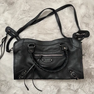 Svart handväska med detaljer  - En cool svart handlväska i skinnmaterial med både axelrem och flätade handtag. 💕 Axelremen är avtagbar! Väskan har silverfärgade metalldetaljer och dragkedja för att stänga ☺️ Perfekt storlek för att få plats med allt du behöver och snygg till alla outfits! Aldrig använd 