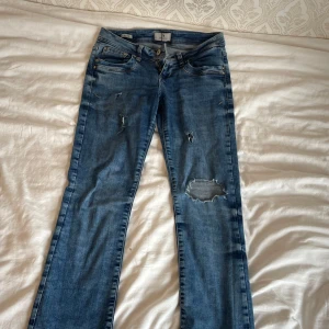 Blå bootcut jeans ITB Valerie W26 L30 - Snygga blå jeans från ITB Blue Addicted, modell Valerie. Bootcut passform med låg midja och slitna detaljer på benen för en cool, avslappnad vibe. Klassisk femficksdesign och dragkedja. Perfekta för dig som gillar en trendig och bekväm stil.