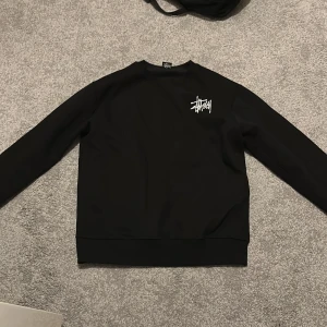 Svart Stüssy sweatshirt XL - Svart crewneck sweatshirt från Stüssy i storlek XL. Tröjan har klassisk passform, rund halsringning och Stüssy-logga broderad i vitt på bröstet. Perfekt basic med streetwear-vibe och mjukt material som känns skönt mot huden.