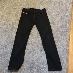 Svarta Diesel jeans straight fit - Säljer ett par svarta jeans från Diesel med klassisk femficksdesign och diskret logga på myntfickan. Jeansen har raka ben och normal passform, perfekta till sneakers eller boots. Materialet är slitstarkt denim i bomull med snygga detaljer på bakfickorna. Storlek W32 och L34