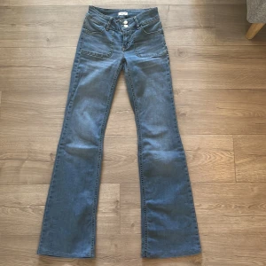Blå lågmidjade bootcut jeans med fickor - Snygga blå lågmidjade jeans med bootcut passform och framfickor. Klassisk femficksdesign med knappar i silver på bakfickorna.
