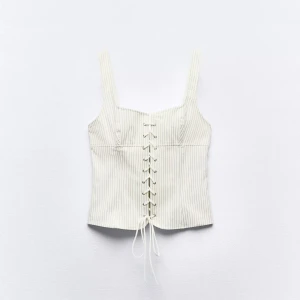 Vit randig korsettopp från Zara  - Supersnygg vit korsettopp från Zara med tunna svarta ränder och snörning framtill. Endast använd när jag testade i butik, säljer pga att den tyvärr ej kommit till användning. Går ej att få tag på på hemsidan längre! Toppen har breda axelband, dragkedja i ryggen och är croppad. Materialet är mjukt och känns lyxigt, perfekt för att lyfta din outfit💞