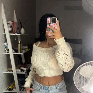 Croppad offshoulder stickad tröja - Säljer en croppad offshoulder stickad tröja i ljus beige med snyggt hålmönster och bred ribbad kant. Tröjan har långärmade ärmar och en loose passform som ger en chill vibe. Perfekt att matcha med jeans för en trendig look.