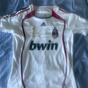 AC Milan Maldini Champions League tröja - AC Milan bortatröja från Champions League-finalen 2007 i Aten, med Maldini 3 på ryggen. Vit med röda och svarta detaljer, Adidas-logga och broderat klubbmärke. Tillverkad i lätt och ventilerande material, klassisk passform och korta ärmar.
