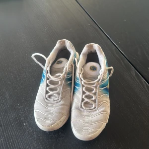 Nike Air Max vita och blå - Nike Air Max Plus sneakers i vitt och blått med coola vågiga detaljer och gula TN-loggor. Skorna har snörning, platt sula och synliga Air Max-enheter i sulan. Materialet är syntet och mesh för skön ventilation. Perfekt för dig som gillar retrostil och streetwear.