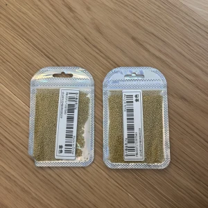 Guldiga pärlor i påse - Två förpackningar med små guldiga pärlor perfekta för kreativa sminklooks eller nageldekorationer. Pärlorna kommer i återförslutningsbara silvriga påsar och är lätta att applicera för att skapa detaljerade och unika effekter. Aldrig använt!! Pris kan diskuteras!
