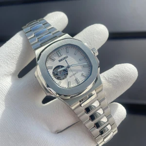 Seiko ”Nautilus” mod - Specifikationer ✨ Modell: Seiko Mod Nautilus Open Heart – Vit urtavla ⚙ Urverk: Pålitligt automatiskt Seiko-urverk (NH38) – inga batterier behövs ⏳ Gångreserv: Upp till 41 timmar 🛡 Boett: Lyxigt bearbetat rostfritt stål med borstade och polerade ytor 📏 Storlek: Elegant 40 mm boett (passar både vardag och fest) 💎 Glas: Reptåligt safirglas med antireflexbehandling 🎯 Urtavla: Vit med sofistikerat rutmönster och fascinerande open-heart-fönster