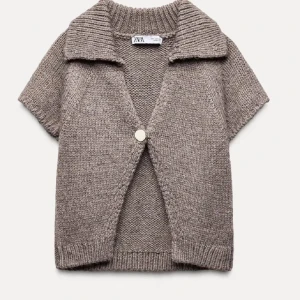 Beige stickad kofta från Zara - Säljer en beige stickad kofta från Zara med korta ärmar och bred krage. Koftan har en knapp framtill och är gjord i mjukt stickat material som ger en chill och avslappnad vibe. Perfekt att slänga över en t-shirt för extra stilpoäng.