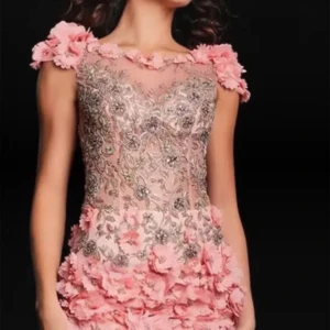Rosa blommig kortklänning med paljetter - Superfin Jovani klänning i ljusrosa med blommiga 3D-applikationer på axlar och nederdel. Klänningen har glittriga paljettdetaljer och broderier över hela framsidan, samt en transparent mesh upptill. Perfekt för dig som vill sticka ut med en unik look! Storlek S men passar perfekt för de som har XS