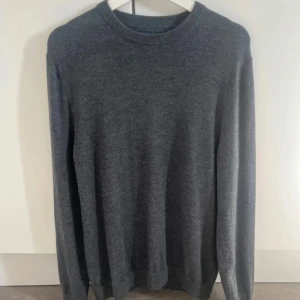 Grå merinoulltröja These Glory Days - Snygg grå stickad tröja från These Glory Days i mjuk merinoull. Klassisk rund hals och långärmad modell med ribbade muddar. Perfekt för dig som gillar stilrena och bekväma plagg. Passar till jeans eller chinos för en chill look.