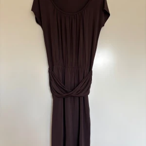 Marella brun midilång klänning (under knä) med drapering runt midjan  - Marella brun midilång klänning (under knä) med drapering runt midjan. U- ringad och korta ärmar. Elegant drapering runt midjan. Tillverkad i högkvalitativ viskos som faller fint. Nyskick! Använd en gång 