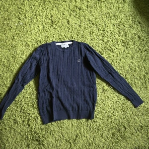 Marinblå kabelstickad tröja  - Snygg marinblå kabelstickad tröja. Tröjan har långärmade ribbade muddar och är gjord i mjuk bomull som är skön mot huden. Perfekt för dig som gillar klassisk stil med en modern touch.