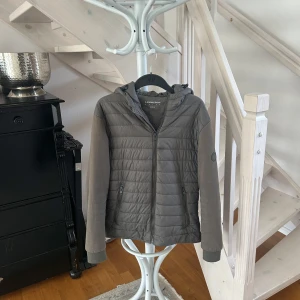 Cardigan från Lindbergh - Snygg grå/grön Cardigan från Lindbergh med huva och dragkedja framtill. Perfekt för kyliga dagar och enkel att matcha med det mesta.